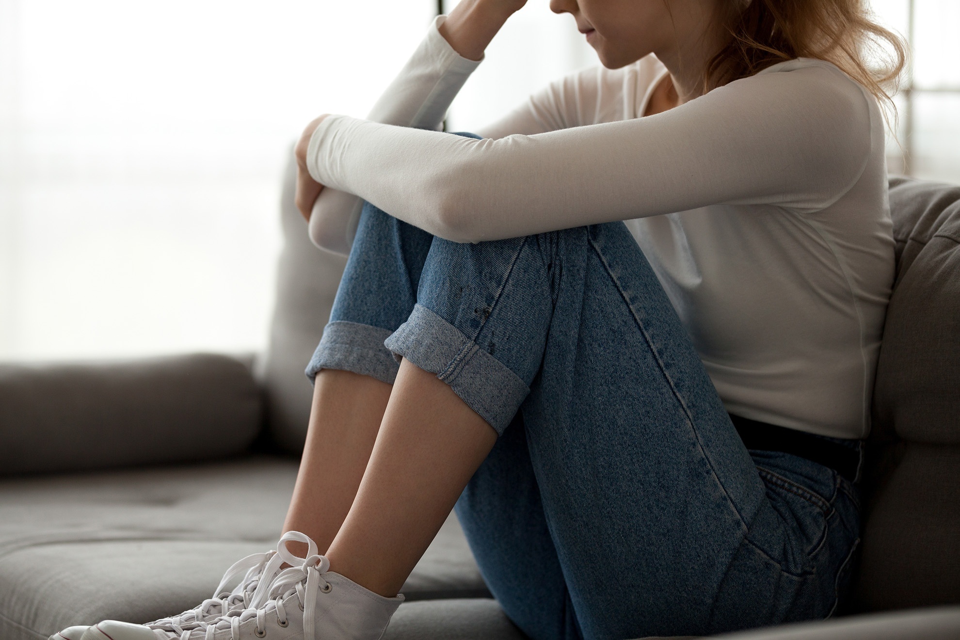 Woman with obvious stress on a couch with one hand to her forehead and the other arm wrapped around her legs.